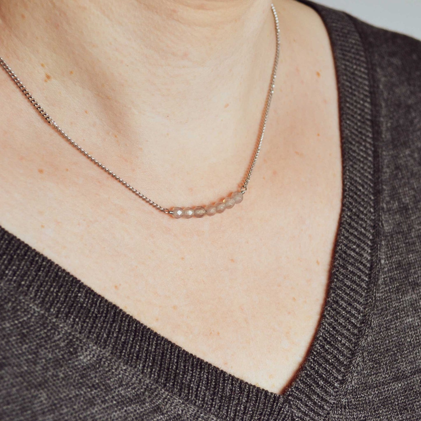 Woman wearing grey v neck jumper and dainty Agate necklace