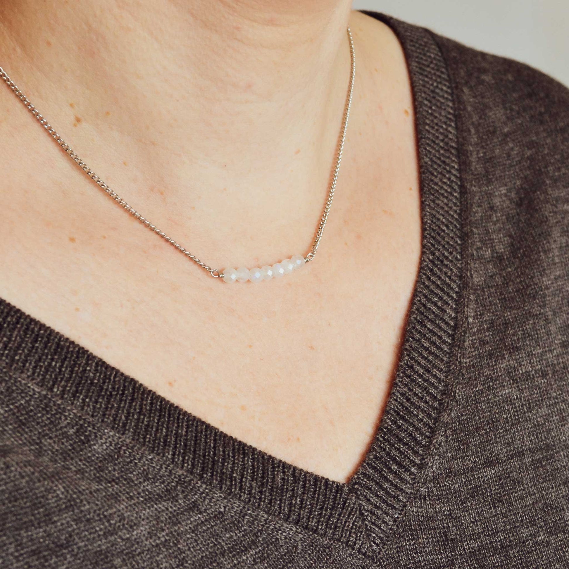 Woman wearing grey v neck jumper and dainty Rainbow Moonstone necklace