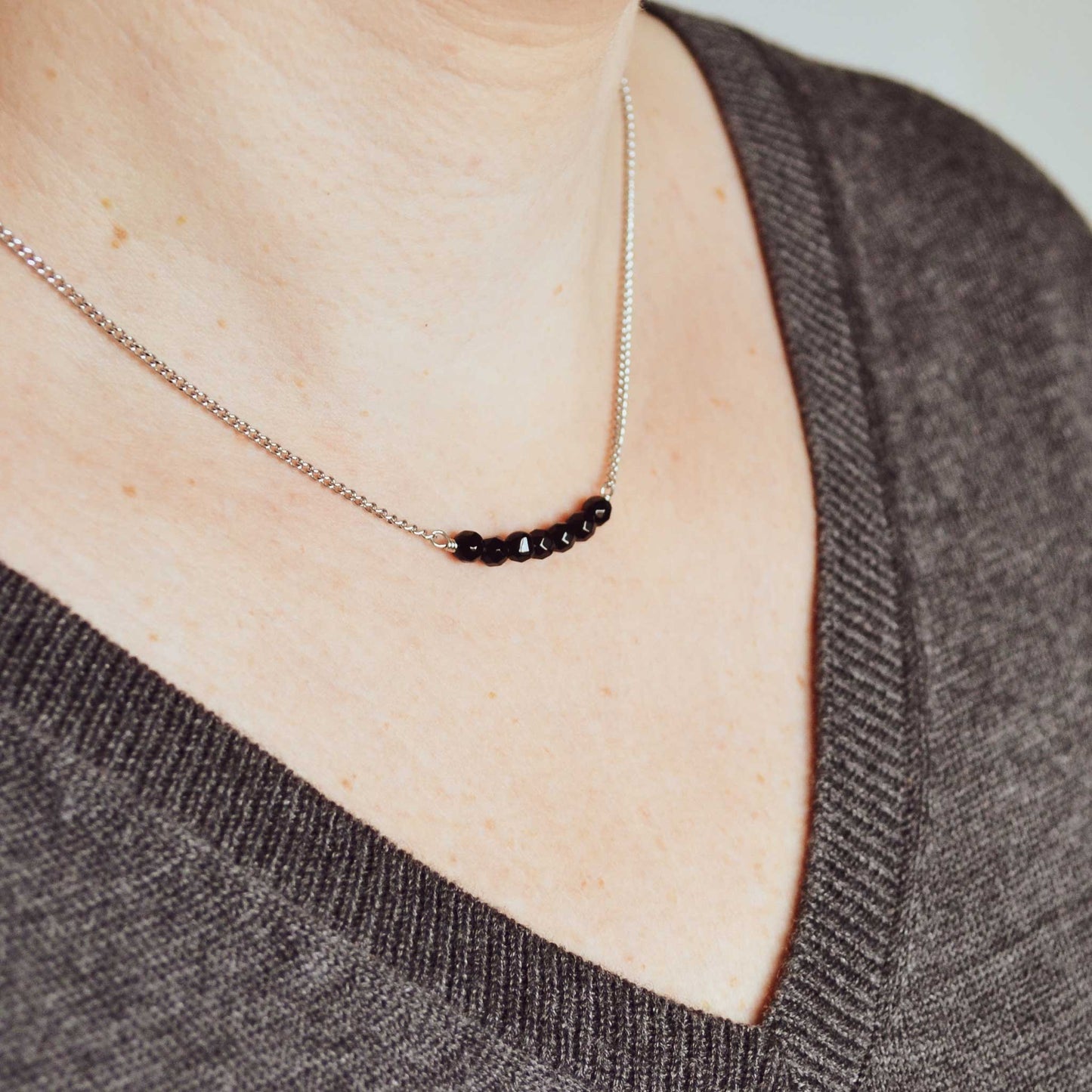 Woman wearing grey v neck jumper and dainty Onyx necklace
