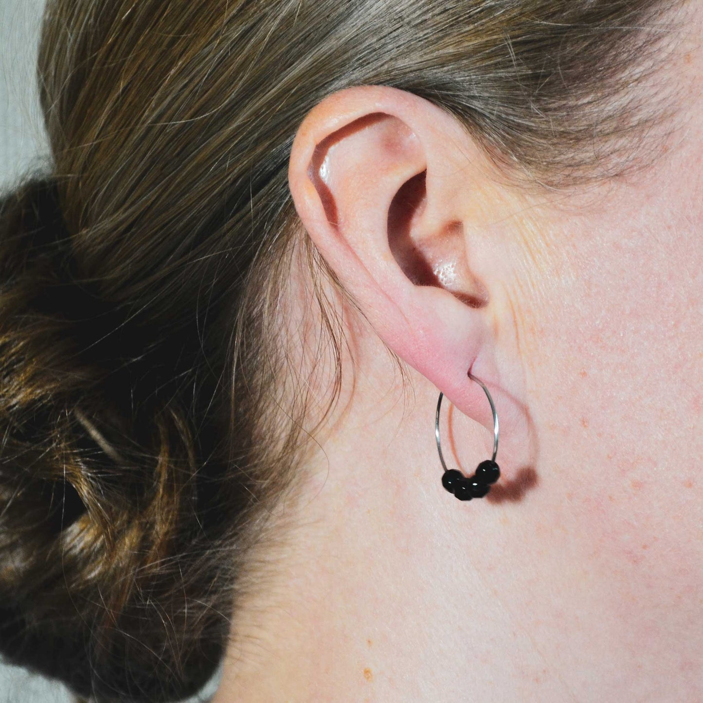 Woman wearing simple Onyx black hoop earring in earlobe
