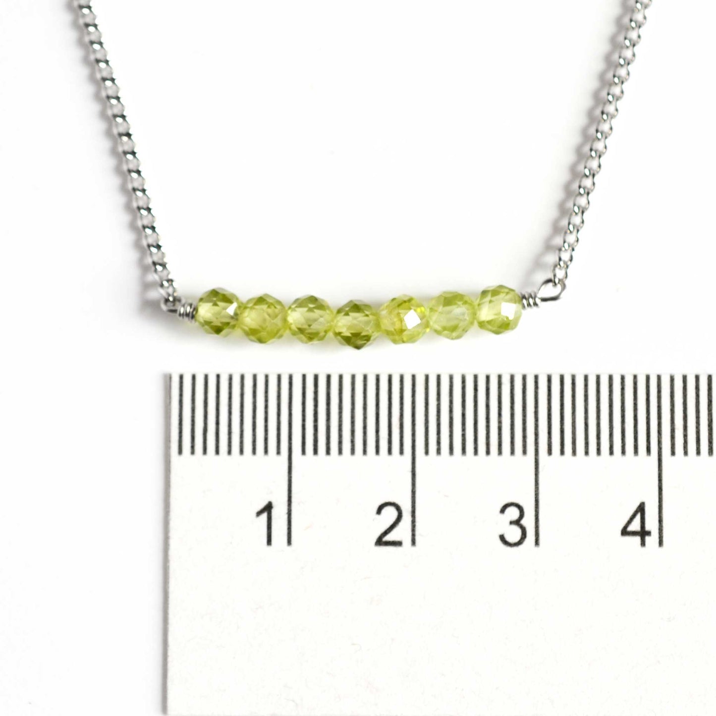 Dainty Peridot bar necklace with 4mm gemstone beads next to ruler