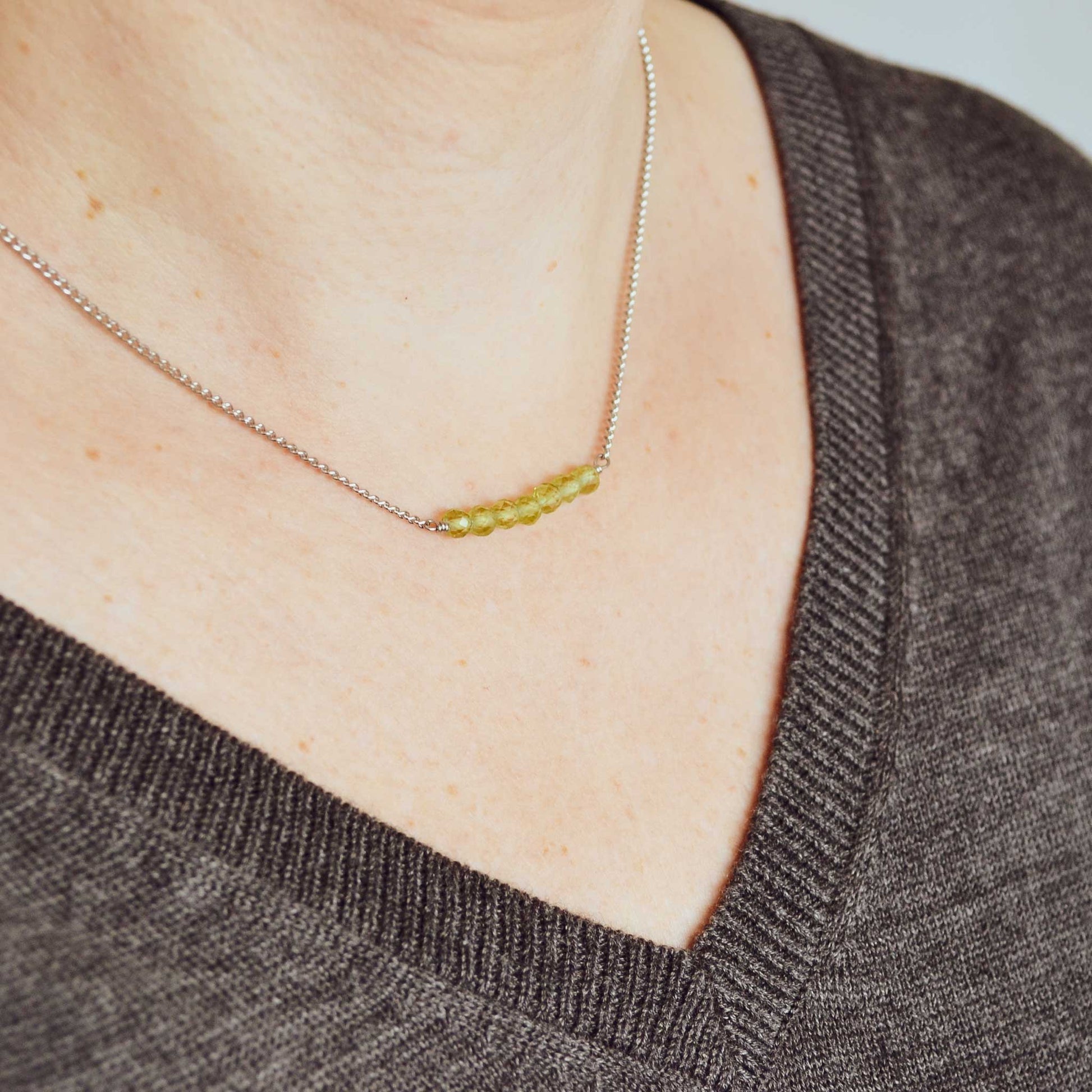 Woman wearing grey v neck jumper and dainty Peridot crystal necklace