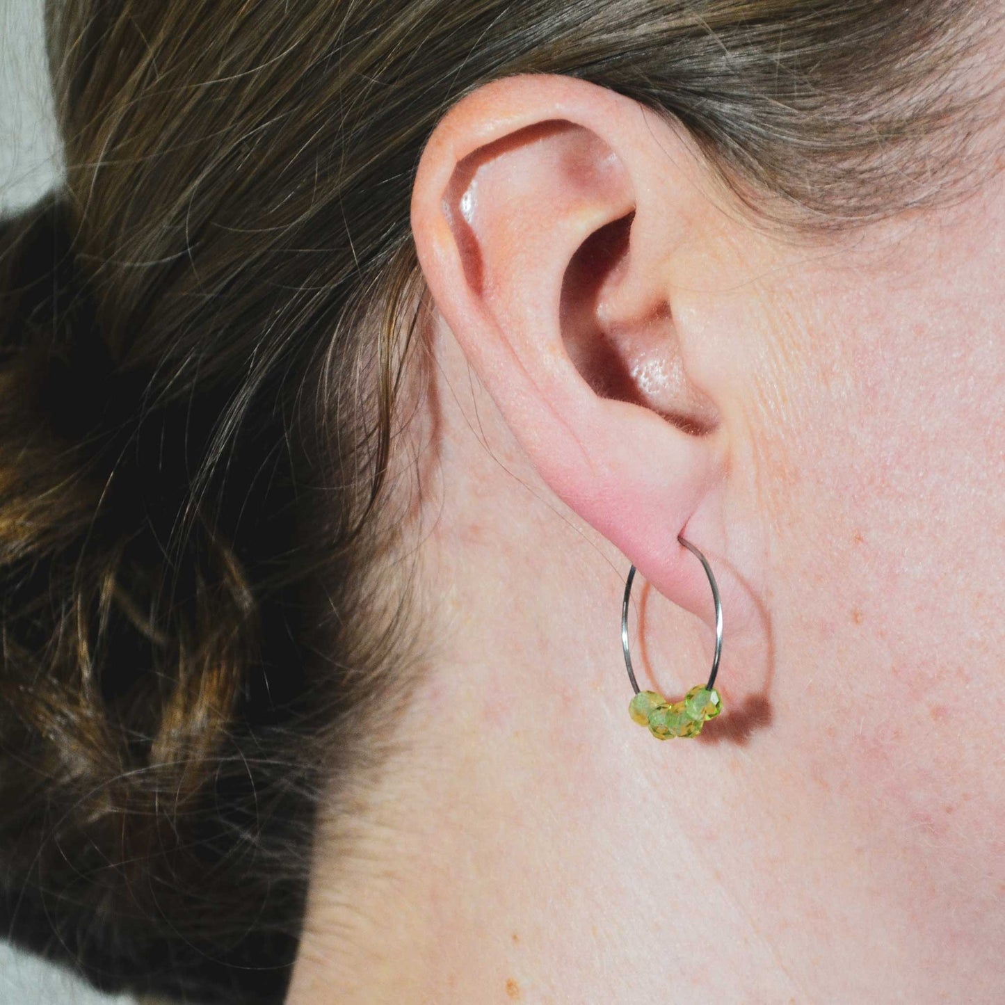 Woman wearing dainty Peridot hoop earrings in earlobe