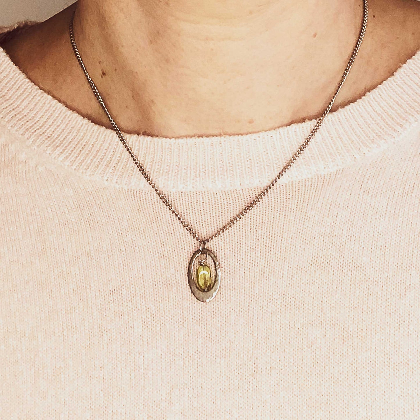 Woman wearing pink jumper and dainty Peridot oval pendant necklace.