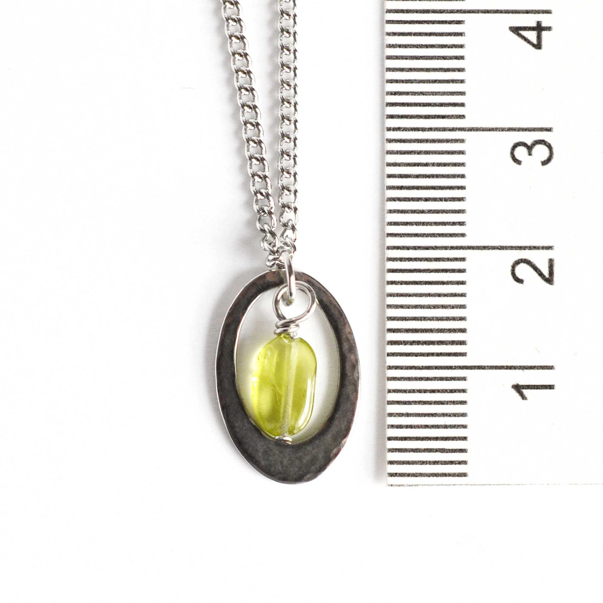 Dainty oval Peridot pendant necklace next to ruler.