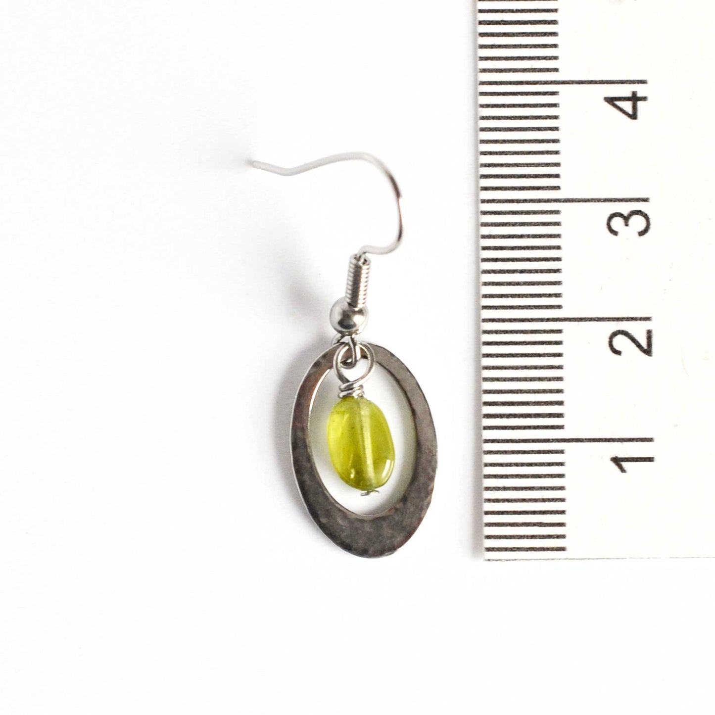 35mm long Peridot and stainless steel oval drop earrings next to ruler.