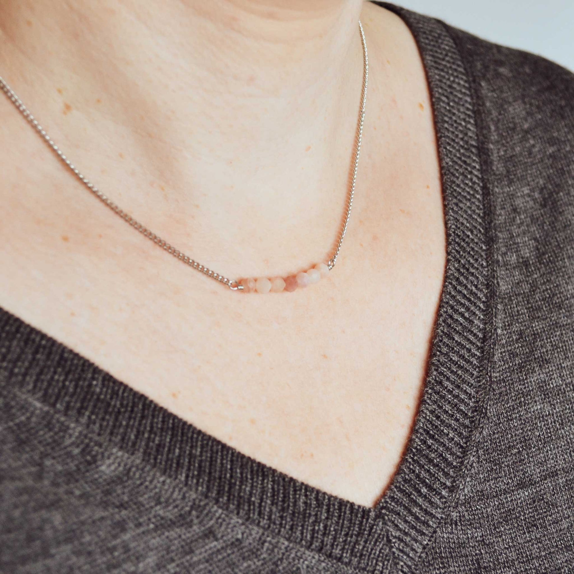 Woman wearing v neck jumper and dainty Pink Opal necklace