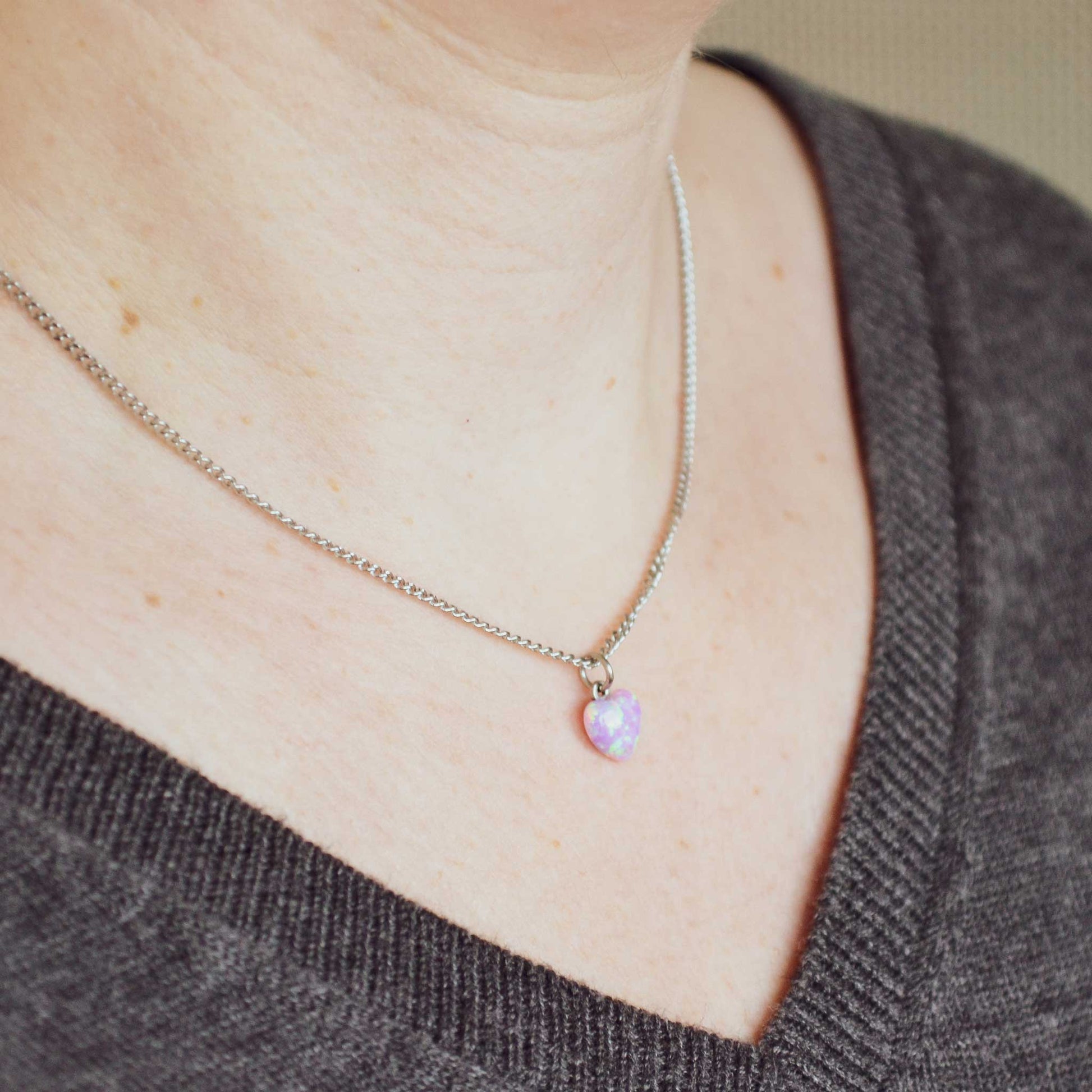 Woman wearing grey v neck jumper and dainty pink heart necklace