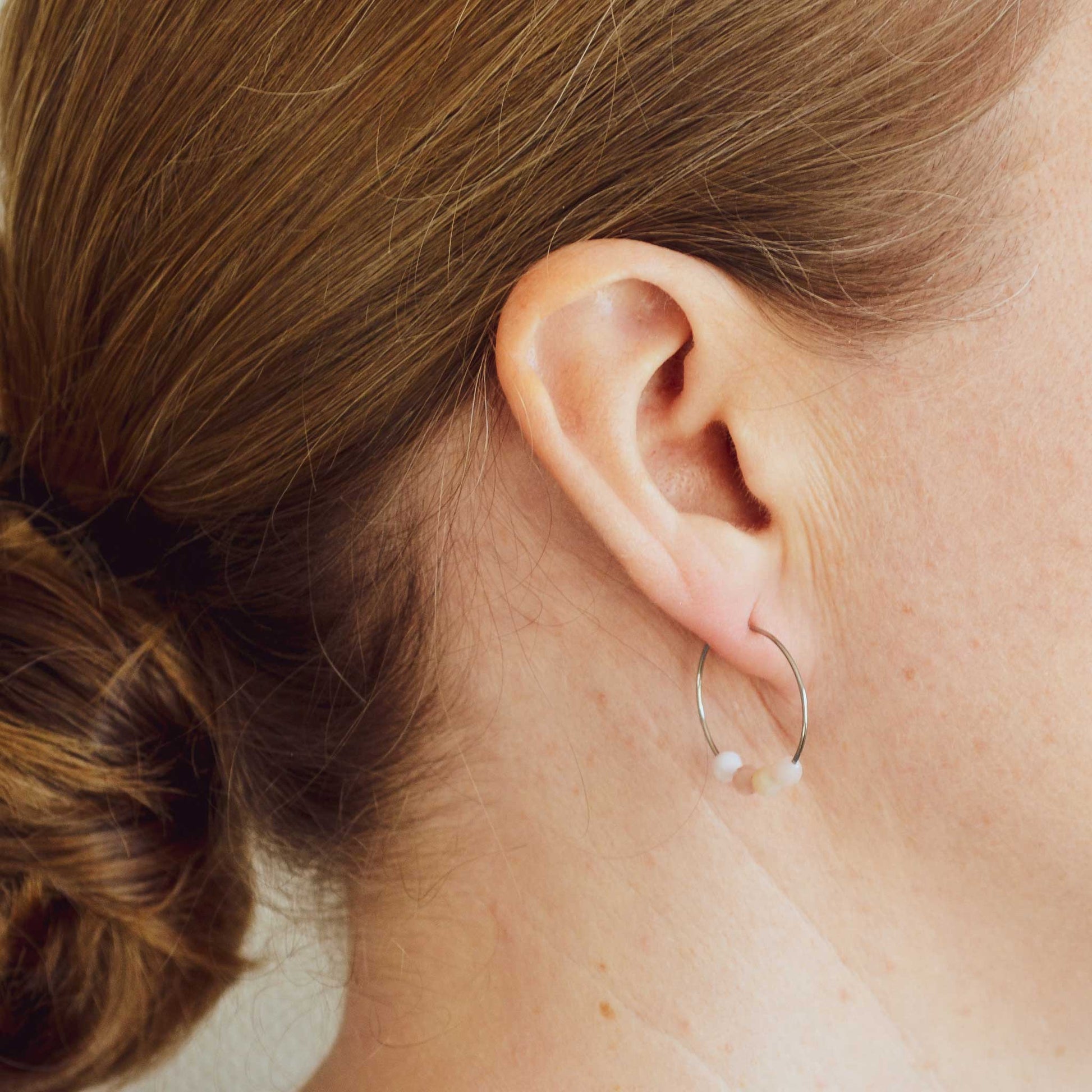 Woman wearing dainty Pink Opal hoop earrings in earlobe