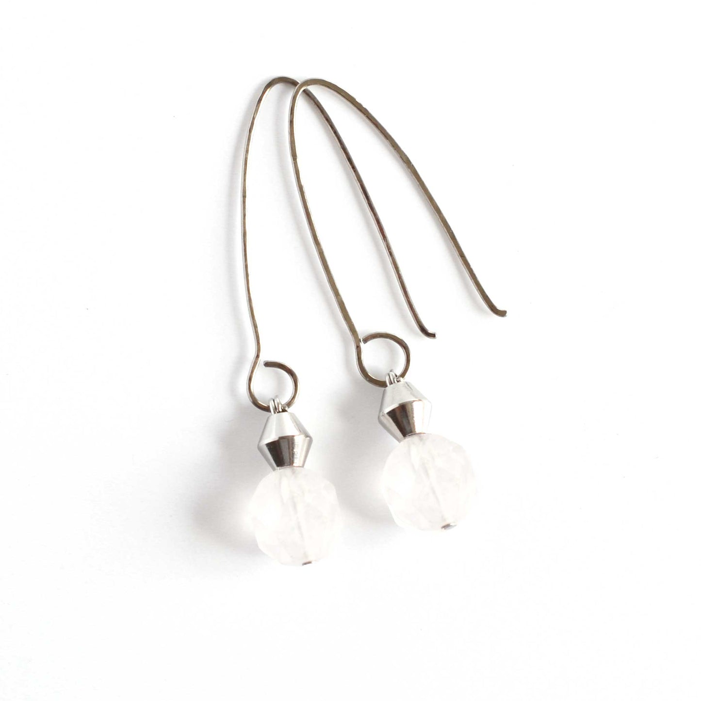 Pale pink Rose Quartz crystal drop earrings with curved hook laying on white background.