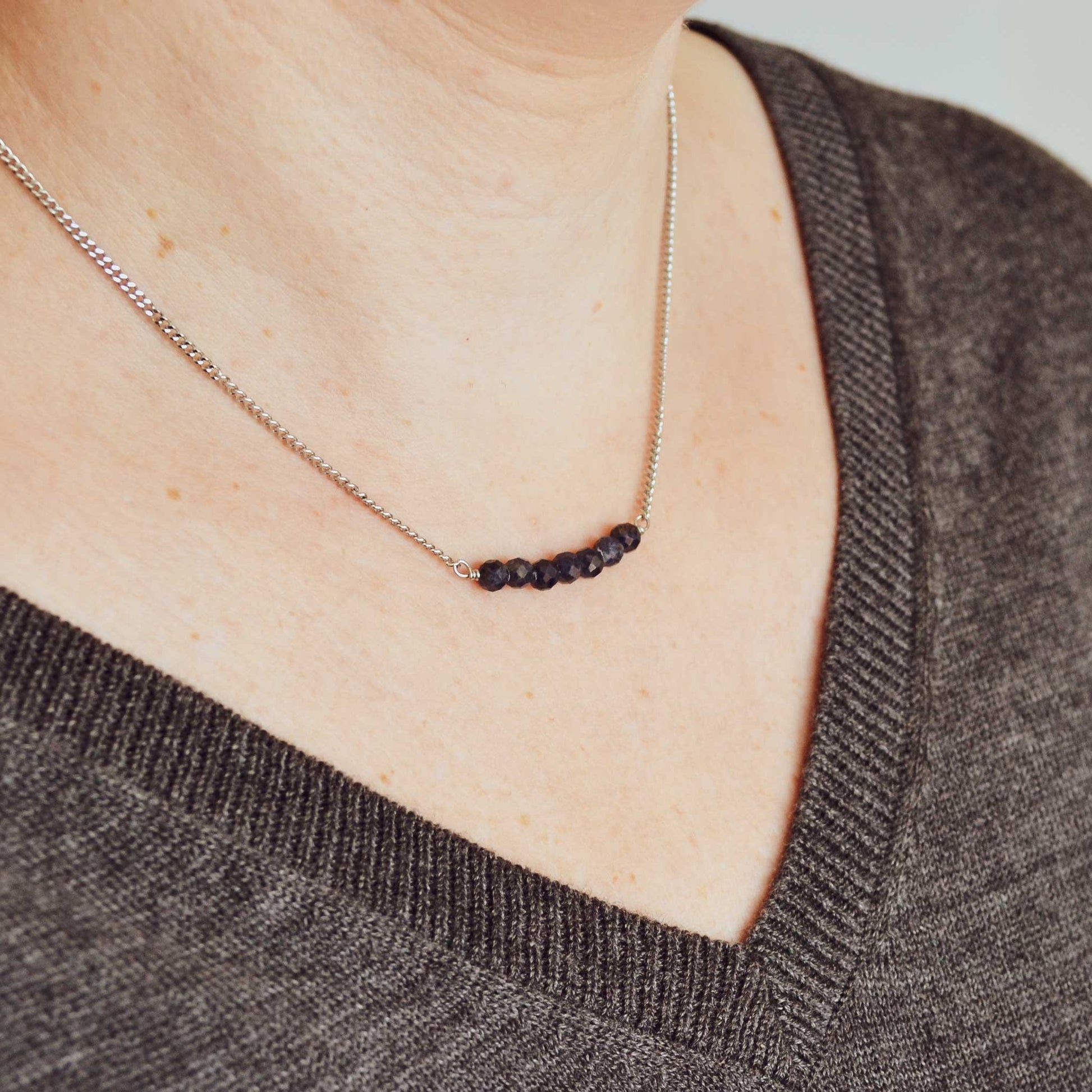 Woman wearing grey v neck jumper and dainty dark blue Sapphire necklace