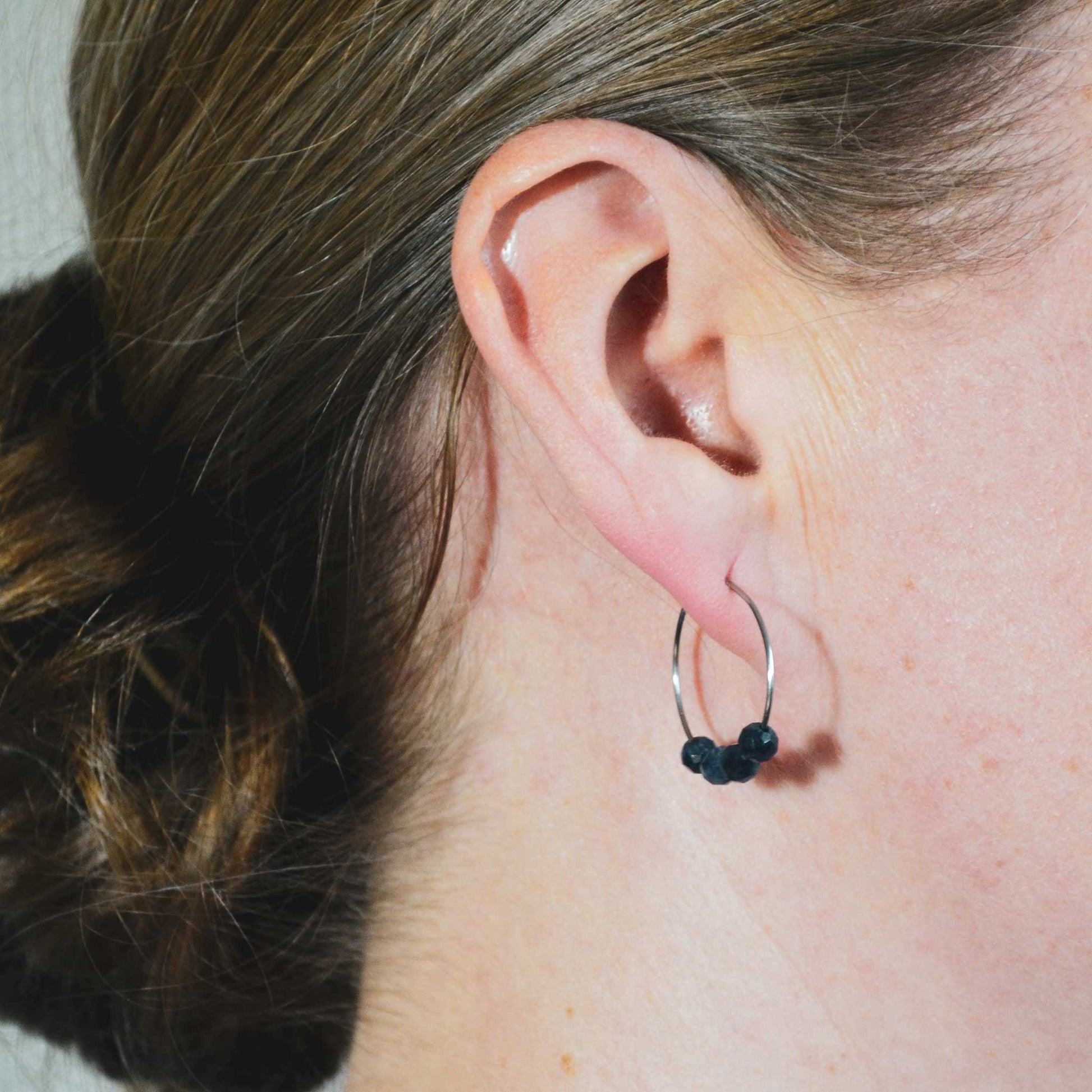 Woman wearing dark blue Sapphire gemstone hoops in earlobe