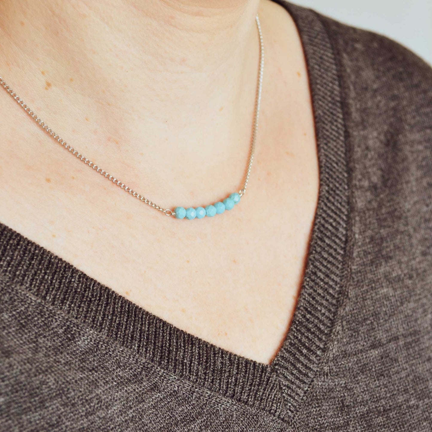 Woman wearing grey v neck jumper and dainty Turquoise bar necklace