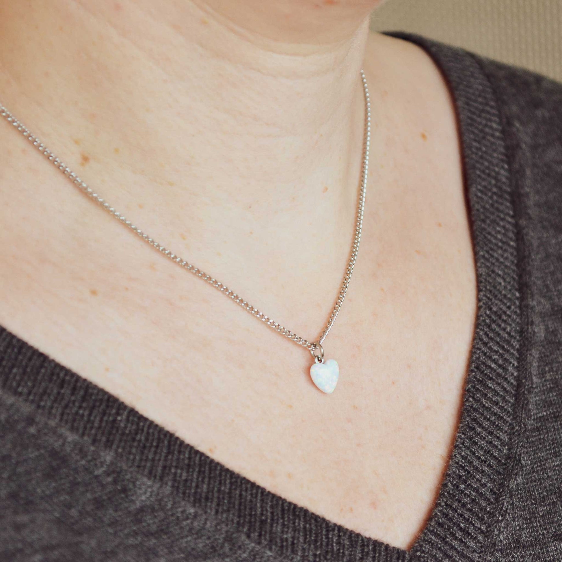 Woman wearing grey v neck jumper and dainty white Opal heart necklace